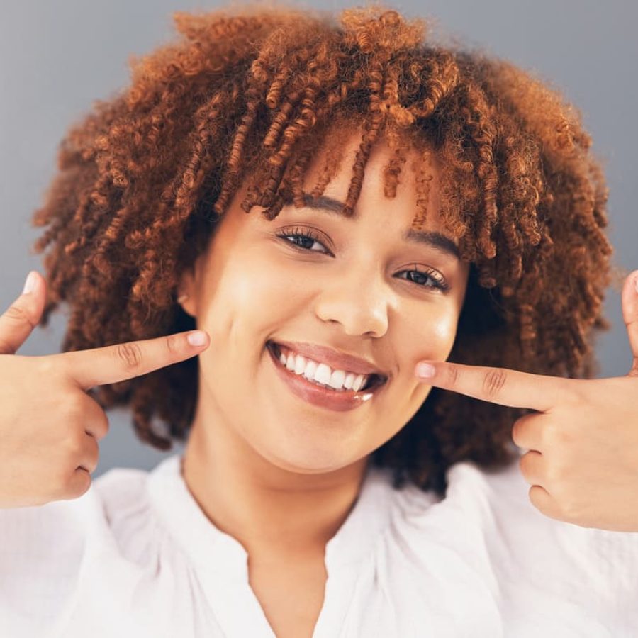 portrait-point-teeth-with-black-woman-smile-oral-hygiene-against-grey-studio-background-face-african-american-female-lady-with-gesture-mouth-happiness-dental-health-wellness